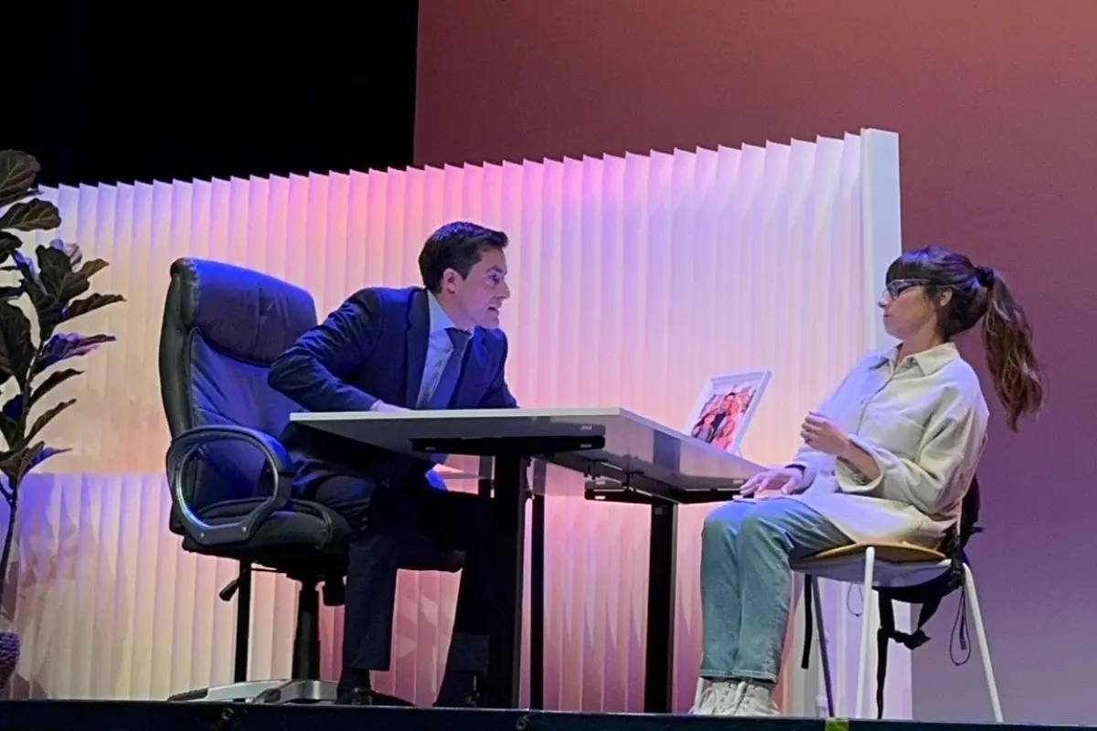 Protagonistas de la obra de teatro El Crédito dialogando intensamente sentados frente a un escritorio.